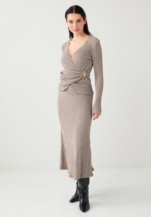 Beżowy, dziergany dwuczęściowy strój z kopertowym topem z złotym akcentem oraz długą, dopasowaną spódnicą sięgającą kostek.