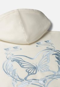 Crème-kleurige hoodie met blauwe geborduurde vlinder- en bloemontwerpen. Zachte textuur met een kangoeroezak en capuchon.