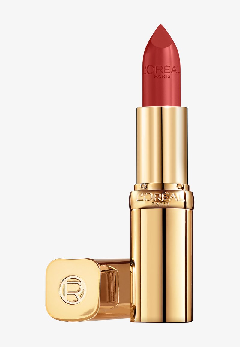 Rouge à lèvres dans un étui en métal doré, avec une forme de bullet arrondie et le nom de la marque gravé. Le capuchon a un coin arrondi avec un logo.