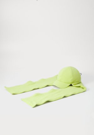 Neon green knitted cap with long integrated scarf laid flat on a white surface.