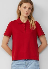 Polo rouge avec une patte de boutonnage et des manches courtes, fabriqué en tissu doux. Design simple, avec un col classique et une coupe décontractée.