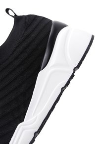 Black knit slip-on sneaker with white chunky sole and pull tab at heel, featuring textured patterns on the upper fabric.