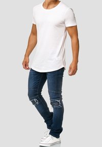Camiseta blanca de cuello redondo, de manga corta, combinada con unos vaqueros ajustados de color azul oscuro con detalles de desgaste en las rodillas y zapatillas blancas.