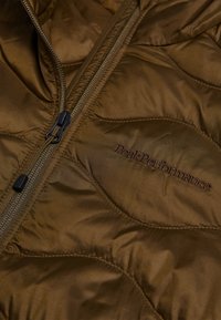 Giacca imbottita marrone con chiusura a zip, logo ricamato "Peak Performance" e una texture di tessuto liscia e lucida.