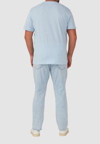 Lichtblauw, korte mouwen t-shirt gemaakt van een zachte stof, gecombineerd met lichtblauwe denim jeans en witte sneakers, bekeken vanaf de achterkant.