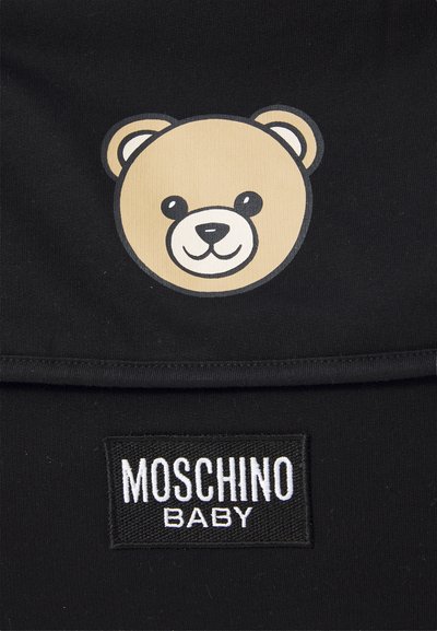 Smaidoša teddy bear seja grafika virs melna plākšņa ar baltu izšūtu tekstu "Moschino Baby" uz melna auduma.