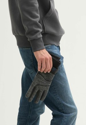 Gray base layer gloves with textured knit, featuring rubber accents on fingers, held in hand alongside black mobile phone, worn with jeans.