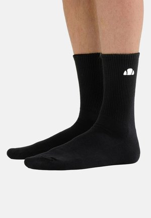 Schwarze, bis zur Mitte der Wade reichende gerippte Socken, getragen an Beinen, mit einem kleinen weißen Logo außen an jeder Socke nahe dem oberen Rand.