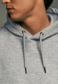 Gray hoodie made from soft fabric, featuring a drawstring hood with black metal eyelets, and textured stitching details.