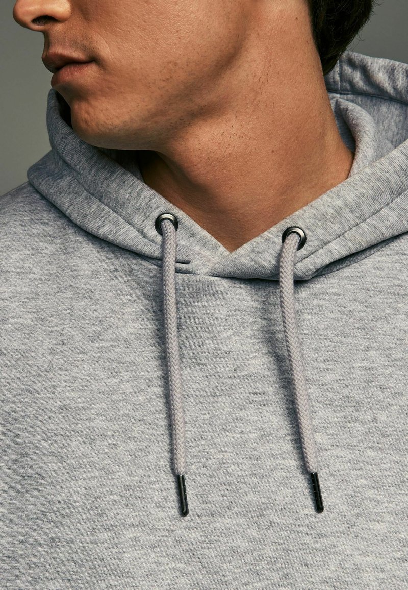 Gray hoodie made from soft fabric, featuring a drawstring hood with black metal eyelets, and textured stitching details.