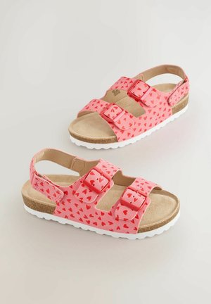 Roosa sandaalid südamekujundustega, kahe reguleeritava rihmaga ja pehme tallaga. Talla värv on valge ja sellel on tekstureeritud haardepind.