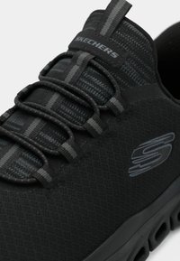Scarpa da ginnastica Skechers nera con lacci elastici, tomaia in mesh traspirante e suola spessa e ammortizzata.