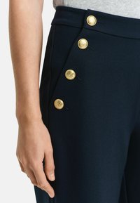 Pantalon marine avec une texture lisse, doté de cinq boutons dorés sur le côté et d'une taille haute ajustée.