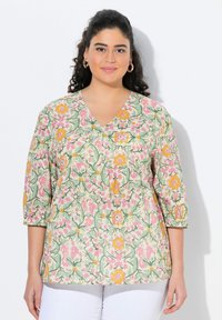 Blusa a fantasia floreale con scollatura a V e maniche a tre quarti. Presenta colori rosa, verde e giallo su uno sfondo crema.