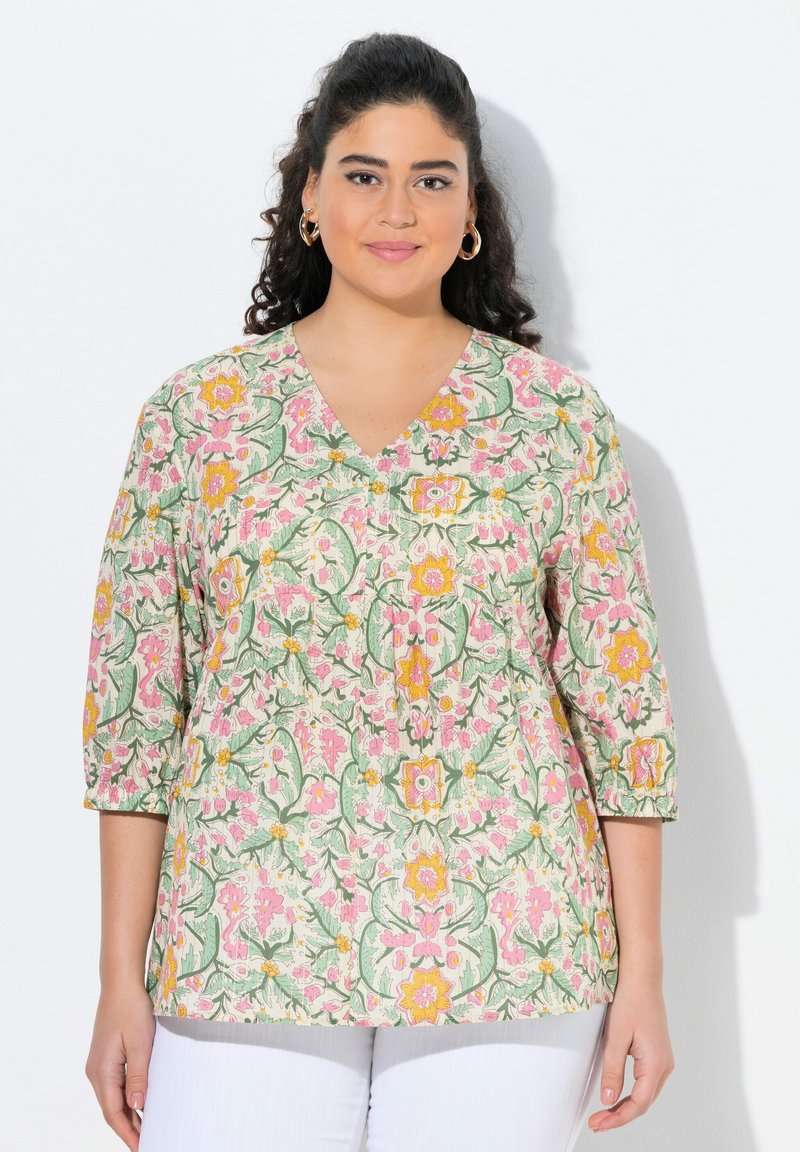 Blusa a fantasia floreale con scollatura a V e maniche a tre quarti. Presenta colori rosa, verde e giallo su uno sfondo crema.