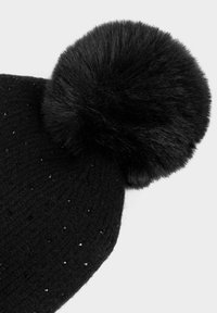Cappello invernale nero a maglia con piccole perline lucenti e un grande pompon in pelliccia sintetica sulla parte superiore.