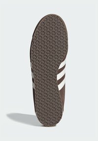 Brun sneakersula med ett texturerat greppmönster. Har tre vita ränder längs sidan och en rundad tådesign.