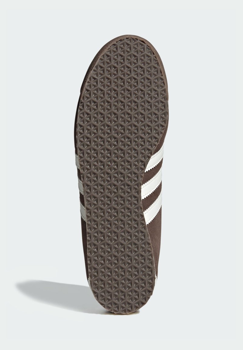 Brun sneakersula med ett texturerat greppmönster. Har tre vita ränder längs sidan och en rundad tådesign.