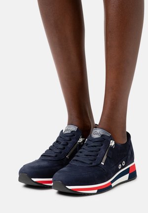 Zapatillas de ante azul marino con un lado con cremallera, cordones de tela y una suela a rayas tricolor con acentos en rojo, blanco y azul.