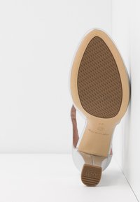 Vue de la semelle d'une chaussure pour femme argentée avec un bout pointu, une semelle en caoutchouc marron texturée antidérapante et un petit talon carré.