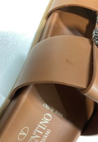 Gros plan sur une sandale slide marron Valentino Garavani avec une large bride et l'inscription « Made in Italy » à l'intérieur.