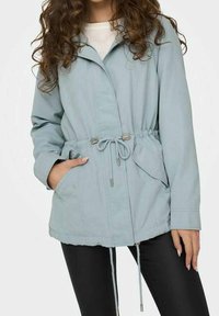 Veste bleu clair avec taille à cordon, fermeture éclair et deux poches latérales. Dotée d'un col et fabriquée dans un matériau doux et lisse.