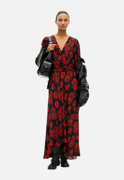 Maxi dress in black fabric with red rose print, featuring a V-neckline and gathered waist. Model carries a black oversized jacket and bag.