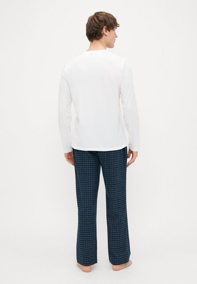 Camisa branca de mangas longas e calças de pijama azuis com um padrão xadrez. As calças são largas, confeccionadas em um tecido macio.