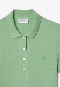 Polo vert en tissu texturé, avec un col, une patte de boutonnage à cinq boutons et un logo de crocodile brodé sur la poitrine.