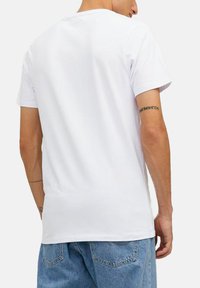Hvid bomulds t-shirt med rund halsudskæring, korte ærmer og en glat tekstur, båret med denim shorts; synlig tatovering på armen.