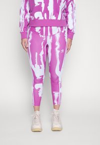 Fialová mikina a legíny s bílými abstraktními vzory. Přiléhavé legíny mají postranní pruhy a malé logo. Nošeno s světlými teniskami.