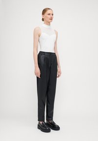 Débardeur blanc sans manches avec un détail côtelé au niveau du col, associé à un pantalon en simili cuir noir et des chaussures noires chunky avec des clous.