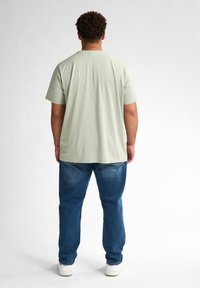 Jasnozielona koszulka z krótkim rękawem z miękkiego materiału, zestawiona z niebieskimi dżinsami i białymi sneakersami, widok od tyłu.