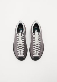 Graue Wildleder-Sportschuhe mit weißen Schnürsenkeln, schwarzem Gummispitzenschutz und Logo an der Seite. Leichtes Design, runde Form, flache Sohle.