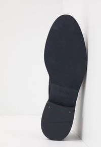 Zwarte rubberen schoenzool met een gestructureerd patroon, een gladde rand en subtiele branding "JOOP!" nabij de hiel, maat 42,5 aangegeven.