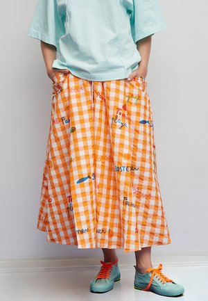 Gonna arancione a quadri con motivi di testo giocosi, tessuto leggero, design plissettato, abbinata a sneakers azzurre con lacci arancioni vivaci.