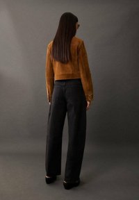 Ruskea mokkakangas lyhyt takki yhdistettynä korkeavyötäröisiin mustiin leveälahkeisiin farkkuihin; yksinkertainen muotoilu ilman näkyviä kuvioita tai varustetietoja.