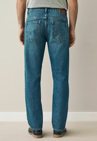 Jeans din denim albastru cu croi drept, având două buzunare pe spate, detalii cusute și un patch din piele pe talie.