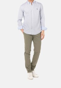 Hellblaues Hemd mit Knopfleiste und feinem Karomuster, hochgekrempelte Ärmel, kombiniert mit olivgrünen Chinos und weißen Turnschuhen.