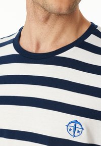 Navy- und weiße gestreifte T-Shirt mit Rundhalsausschnitt, aus Baumwolle gefertigt, mit einem kleinen blauen gestickten Logo auf der linken Brust.