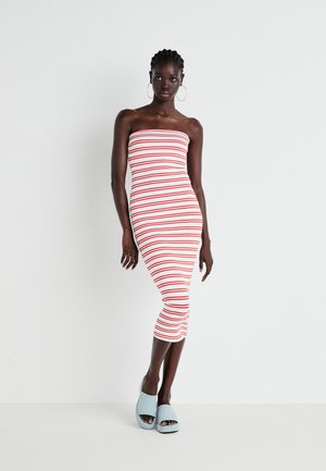 Robe midi sans bretelles, ajustée, blanche avec des rayures horizontales rouges, fabriquée dans un tissu élastique. Le mannequin porte des chaussures à plateforme bleu clair.