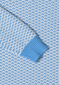 Gros plan sur la manche d'un pull tricoté bleu et blanc texturé avec un poignet côtelé bleu, mettant en valeur un motif géométrique de points et le détail du tissu.