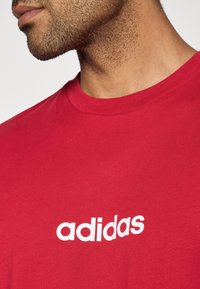 Punane puuvillane T-särk, mille rinnal on valge "adidas" logo, klassikalise ümmarguse kaelusega ja pehme tekstuuriga.