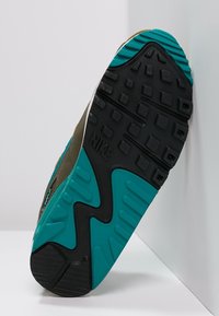 Podešev Nike tenisky s černým dnem a vlněným tyrkysovým mezipodešví, texturovaným vzorkem a logem. Design zahrnuje pryžové akcenty.