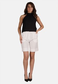 Top nero senza maniche abbinato a pantaloni corti in lino bianchi. I pantaloni corti hanno una vita alta e orli risvoltati, indossati con tacchi alti neri.