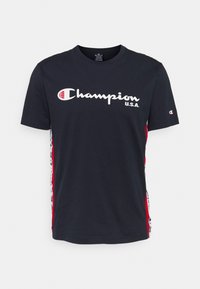 Námořnická modrá bavlněná tričko s bílým logem "Champion U.S.A.", červenými bočními akcenty a černobílým vzorovaným zdobením na bocích.