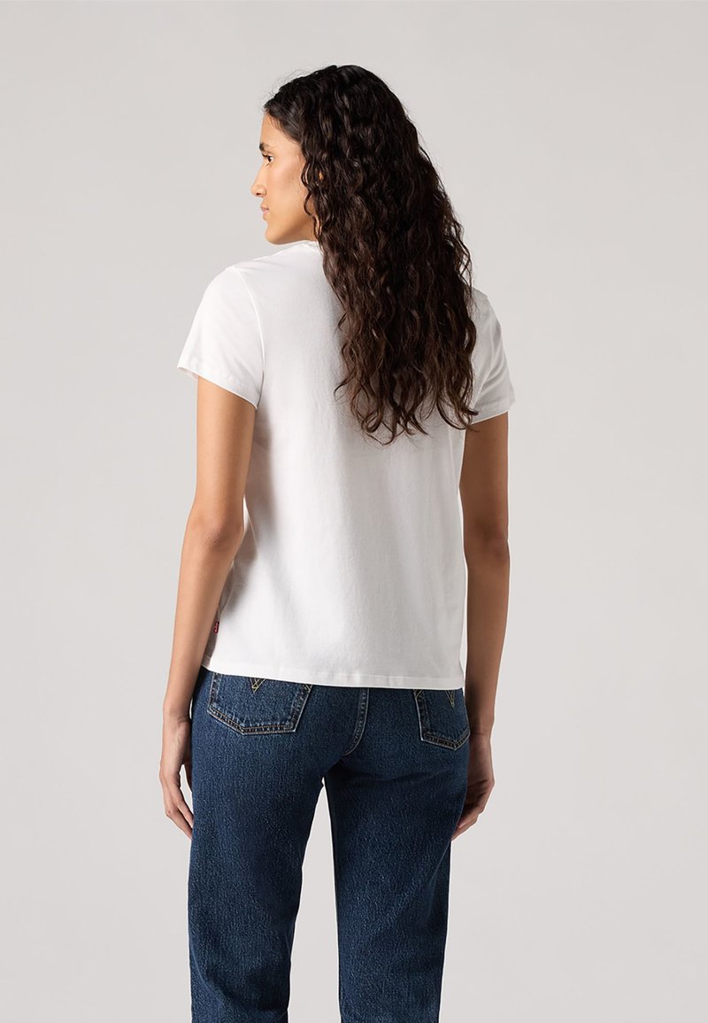 Camiseta de algodón blanca de manga corta, con un corte clásico y un escote redondeado, combinada con pantalones vaqueros azul oscuro con detalles en los bolsillos traseros.