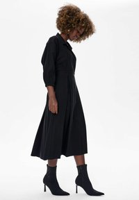 Czarna sukienka midi z krótkimi bufkami, kołnierzykiem oraz plisowanym dołem. Połączona z czarnymi botkami za kostkę z zapięciem na zamek.