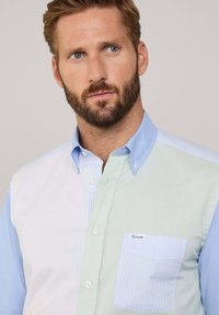 Camisa de hombre de botones con un diseño mitad azul, mitad verde y un bolsillo a rayas en azul claro. Fabricada con un suave tejido de algodón.