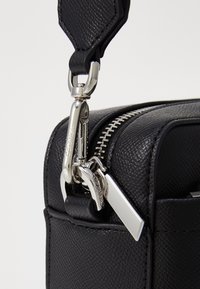 Borsa in pelle nera texturizzata con zip argentata e dettagli in metallo, dotata di un gancio girevole. Design compatto con accenti eleganti.